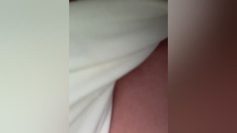 Video of a close-up of a person's thigh with a light tan skin tone, lying on a white bedsheet. The image is slightly blurred, emphasizing texture and softness.