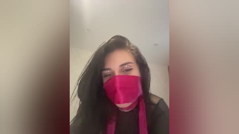 A video of a young woman with long black hair and fair skin, wearing a red face mask, black top, and glittery eye makeup.