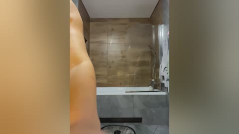 Video of a modern bathroom featuring a beige tiled wall, a white bathtub, a chrome faucet, and a beige towel hanging on a rack.