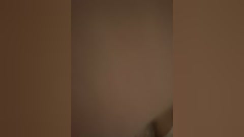 A close-up video of a person's torso, blurred and indistinct, set against a plain, neutral-toned background. The image lacks discernible details, making it difficult to identify specific features or context.