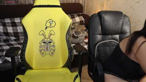Video of a person in a black bra facing a neon-yellow gaming chair with a rabbit face and question mark, set in a cluttered living room with patterned furniture.