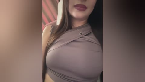 Video of a woman with fair skin, long straight brown hair, wearing a tight, light purple halter top revealing ample cleavage, and bold maroon lipstick. Background features a blurred, striped pattern.