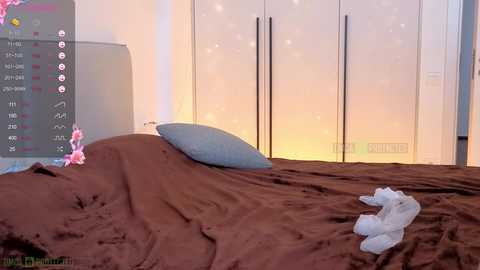 Video of a modern bedroom with a brown bedspread, light blue pillow, white teddy bear, and a digital clock displaying \"11:11\" on the wall.
