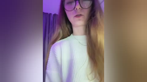 A video of a young woman with long, straight brown hair, wearing large black-rimmed glasses and a white ribbed sweater, standing in a dimly lit room with purple and yellow light accents.