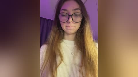 Video of a young woman with long, straight brown hair, wearing black-rimmed glasses, a white ribbed sweater, and a delicate necklace, indoors with purple lighting and blurred background.
