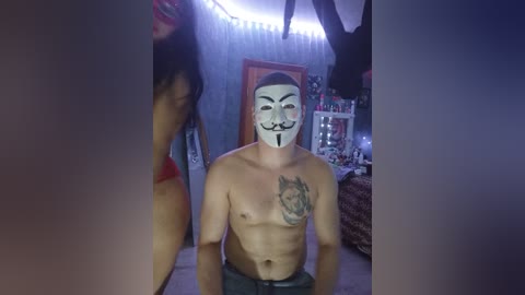 Video of a shirtless, muscular man with a white mask and mustache, standing in a dimly lit room with a wolf tattoo on his chest.
