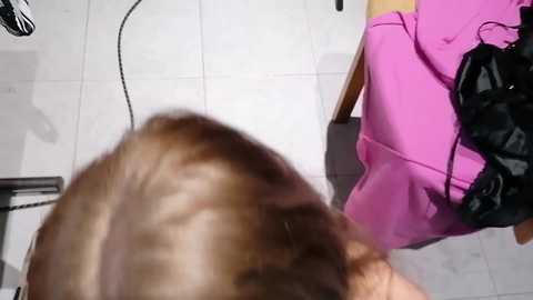 A video shows a brown-haired person in a pink jacket and black gloves bending over to pet a dog on a tiled floor.