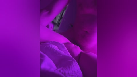 Video of a partially obscured woman lying on a bed, illuminated by vibrant purple lighting, showing her profile with a soft, intimate mood.