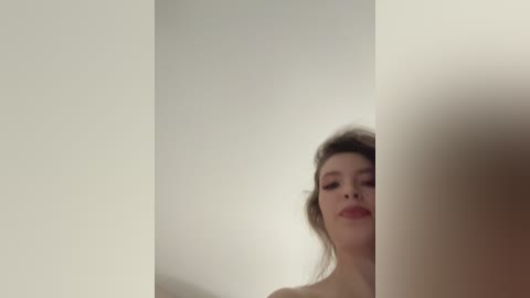 A video of a young woman with fair skin, brown hair, and light makeup, partially obscured by a white wall.