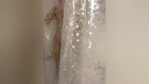 A video of a nude man, viewed from behind, standing in a steamy bathroom. The fogged glass shower door reveals his silhouette and outlines his muscular back and buttocks.