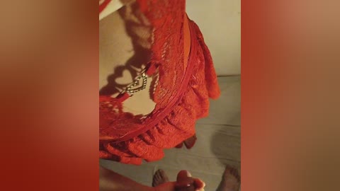 A close-up video of a woman's red lace dress with intricate floral patterns, revealing a glimpse of her beige bra underneath. The background shows a blurred beige wall and light wooden floor.