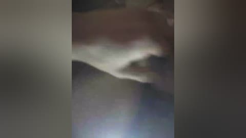 A blurred, dimly lit image featuring a person with dark skin, possibly female, in a dimly lit, possibly outdoor setting, with indistinct surroundings.