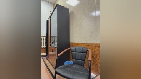 Video of a modern, minimalist room with a black leather chair, a tall black and brown cabinet, and beige textured wallpaper.