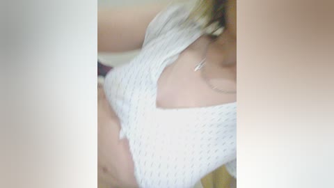 A video of a woman's torso in a white, textured crop top, with her face out of focus. She has fair skin and a slim build, with a small silver necklace visible.