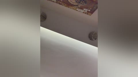 Video of a ceiling with a geometric pattern of light and shadow, showcasing a textured, decorative wall hanging in the top corner. The image is slightly blurred.