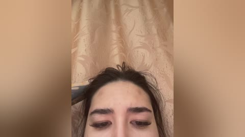 Video of a close-up view of a woman's face with long, dark hair, partially styled with a black hairbrush. Her eyes are closed, and she has thick eyebrows. The background features a beige curtain with a subtle floral pattern.