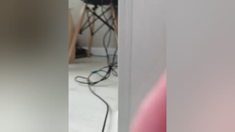 Video of a modern office corner with white walls, a wooden chair, black cables, and a pink object partially visible on the right.