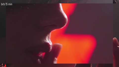 A close-up video of a person's profile, illuminated by a red light, with a time stamp of \"brt 15 min.\" The background is blurred, enhancing the focus on the person's nose and mouth.