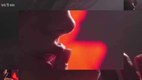 Video of a person with a nose and mouth covered in red paint, set against a blurred, dimly lit background with red and black hues.