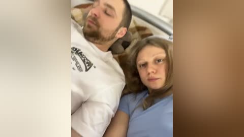 Video of a man and woman in a hospital bed, both asleep; the man wears a white T-shirt, and the woman a blue shirt.