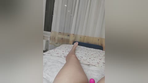 A video shows a nude woman lying on a bed, her legs spread, with a pink vibrator in her hand. The background features a window with sheer curtains and a wooden headboard.