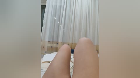 Video of a woman's bare legs and feet, positioned centrally, with sheer white curtains and a wooden chair in the background.