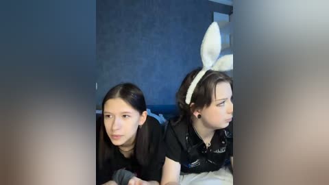A video of two young girls in a bedroom, one wearing a black dress, the other a bunny costume, with a blurred out person in the foreground.
