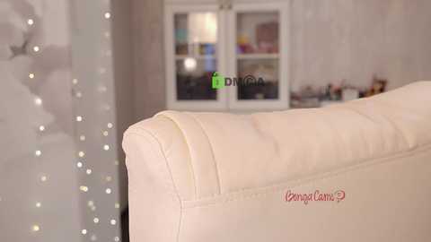 A video of a cream-colored leather sofa with a subtle crease on its armrest. The background features a softly lit room with a white cabinet and decorative items, creating a cozy, elegant atmosphere.