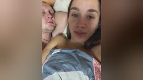 A video shows a sleeping Asian man with fair skin and short hair, lying on his side, next to a sleeping Asian woman with long dark hair, both wearing casual clothes, with a blurred background.