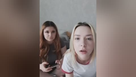 A video of two young women with long hair, one brunette and the other blonde, both in casual t-shirts, taken from a blurry, out-of-focus perspective.