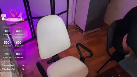 A video showing a modern office chair and a person seated in a dimly lit room with purple ambient lighting, wooden floor, and a standing lamp.