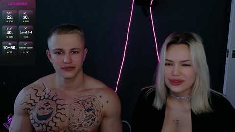 Video of a shirtless, muscular young man with intricate tattoos and a blonde woman in a black top, both smiling, set against a dark, neon-lit background.