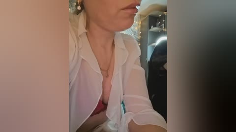 Video of a woman in a white lab coat, pink bra, and necklace, taken indoors with blurred background.