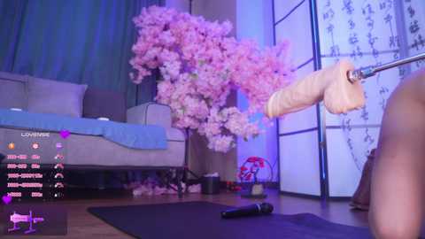 A digital photo of a VR scene showing a nude man with an erect penis, surrounded by pink cherry blossoms, in a modern living room with a sofa and a shoji screen.