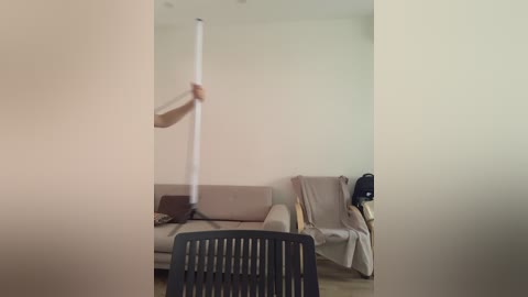 Video of a minimalist living room with a beige sofa, a white ceiling fan being installed, and a black chair in the foreground.