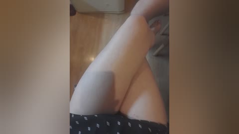 Video of a light-skinned woman's legs in black panties, lying on a wooden floor, with a grey blanket visible in the background.