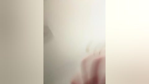 A blurry video featuring a hand with a tattoo, partially visible in a light-colored room. The image is out of focus, making it difficult to discern details.