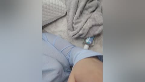 A video of a close-up view of a person's upper body, partially dressed in a light blue shirt, with a grey, textured blanket draped over them. The image is slightly blurred, making details indistinct.