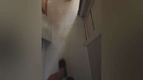 Video of a narrow, dimly lit hallway with beige walls, a person running towards the camera. The hallway leads to a wooden door on the right.