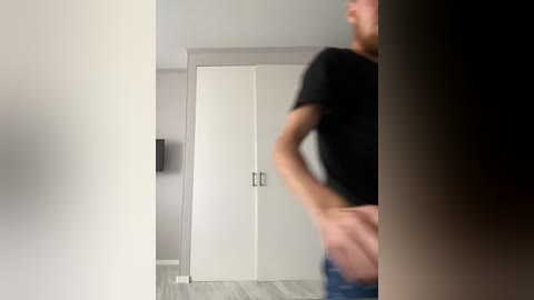 A blurry video of a man in a black t-shirt and jeans, standing in a modern, minimalist room with white walls and a gray door.