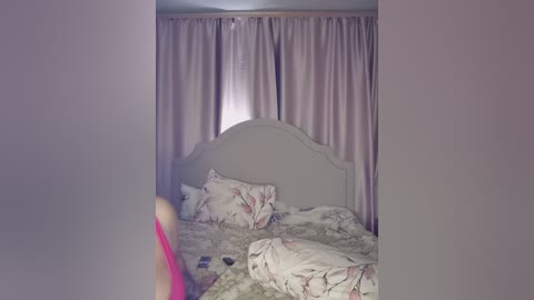 A video of a cozy bedroom with a white headboard, floral-patterned bedspread, and soft pink curtains. The room is dimly lit, and the image is slightly blurred, emphasizing a warm, intimate atmosphere.