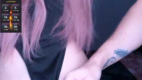 Video of a person's hands and shoulder with pink hair, wearing a black top, and visible tattoos, overlaid with a digital timer showing 1:15.