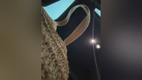 A video captures the textured weave of a straw handbag with a beige strap, set against a dark background with a bright spotlight on the right.