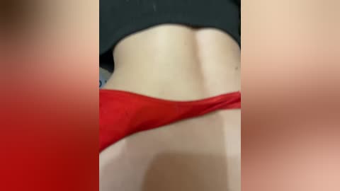 A close-up video of a woman's lower back and buttocks, wearing red thong underwear and a black crop top. The image is blurry with a red and black gradient filter.