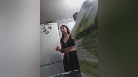 A video of a young woman with long brown hair, wearing a black bra and sweatpants, standing in a dimly lit, narrow hallway, framed by a mirror on the right.