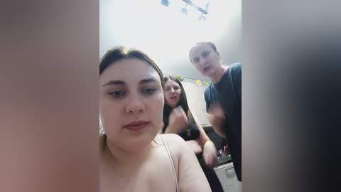Video of three women in a bathroom, one in the foreground with a neutral expression, the other two in the background smiling.