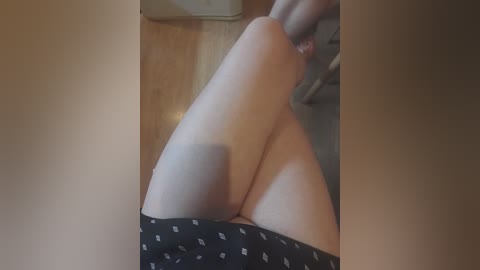 A video of a person's legs in black polka-dotted shorts, seated on a wooden floor with a blurry background.