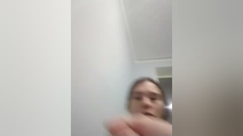 A blurry video of a young woman with light skin and brown hair, partially obscured by a white wall, possibly taken in a bathroom.
