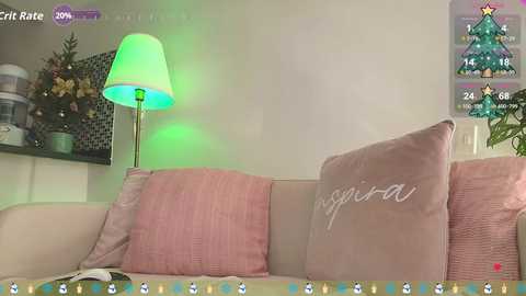 Video of a cozy living room with a beige couch adorned with pink and white cushions, a green-lit lamp, a decorated Christmas tree, and a virtual Christmas tree game overlay.