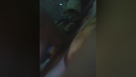 A dimly lit, close-up video of a person's hand with a black glove on the right, partially obscured by a blurry, dark background. The gloved hand appears to be holding or touching something, possibly a gun.